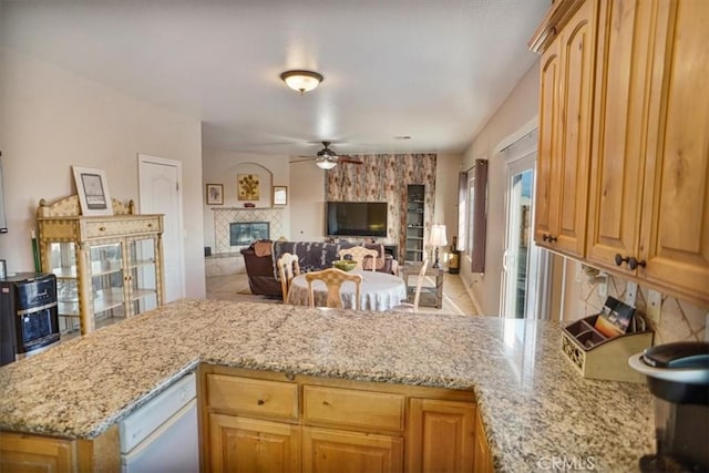 kitchen with a ceiling fan, open floor plan, a peninsula, a fireplace, and light stone countertops