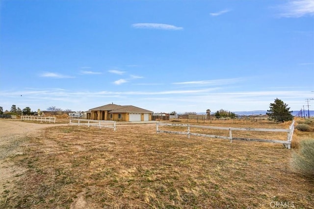 view of yard featuring a rural view, an attached garage, and fence