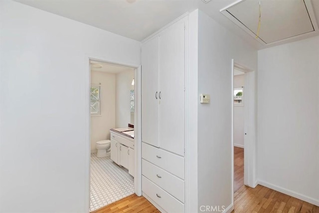 hall with attic access, baseboards, and light wood-type flooring