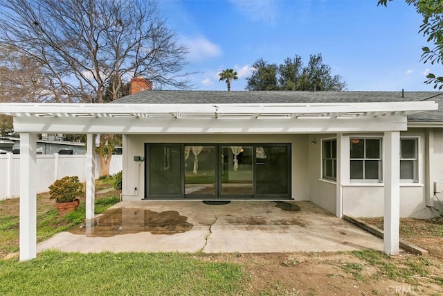 rear view of house with stucco siding, a patio, fence, a shingled roof, and a chimney