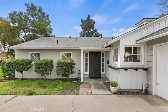 entrance to property featuring stucco siding, board and batten siding, and a shingled roof