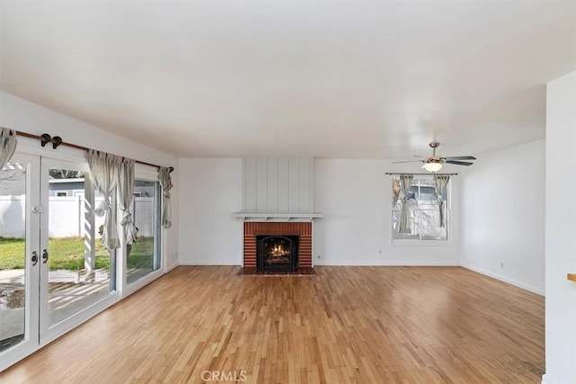 unfurnished living room with light wood-style floors, a brick fireplace, and a ceiling fan