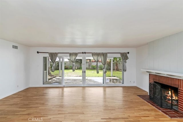 unfurnished living room with visible vents, baseboards, a brick fireplace, and wood finished floors