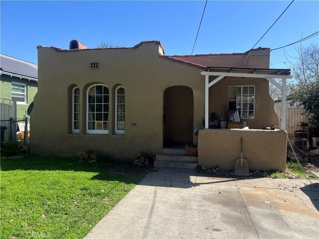 view of front of house with stucco siding, a patio area, a front lawn, and fence