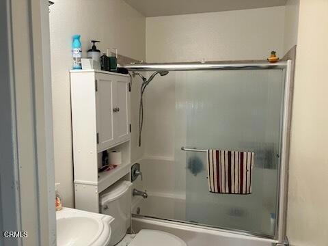 bathroom featuring toilet and bath / shower combo with glass door