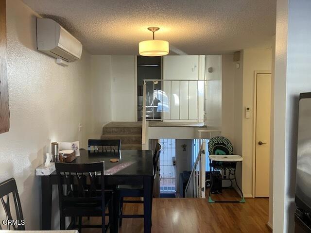 dining space featuring stairway, a textured ceiling, a wall mounted AC, and wood finished floors