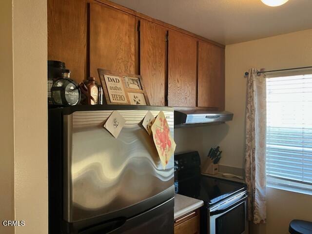 interior space with range hood, brown cabinets, and appliances with stainless steel finishes