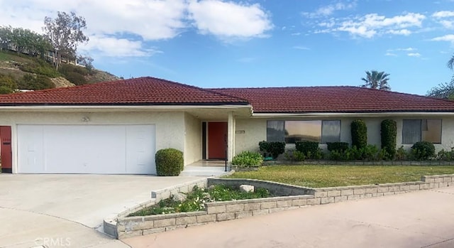 view of front of property featuring a tiled roof, concrete driveway, a front yard, stucco siding, and a garage