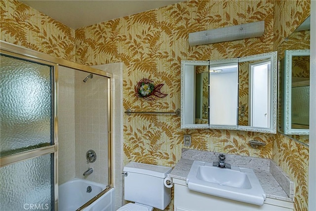 bathroom featuring toilet, wallpapered walls, vanity, and bath / shower combo with glass door