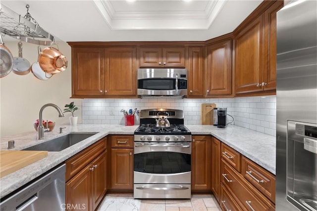 kitchen featuring crown molding, a tray ceiling, decorative backsplash, appliances with stainless steel finishes, and a sink