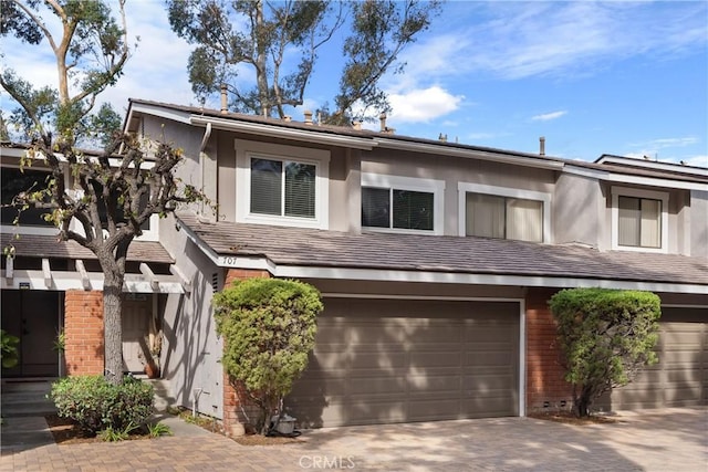 townhome / multi-family property with stucco siding, driveway, brick siding, and an attached garage