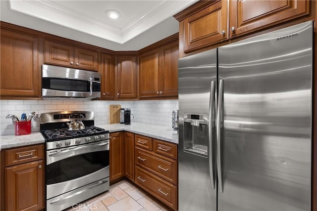 kitchen featuring ornamental molding, tasteful backsplash, stainless steel appliances, a raised ceiling, and light stone countertops