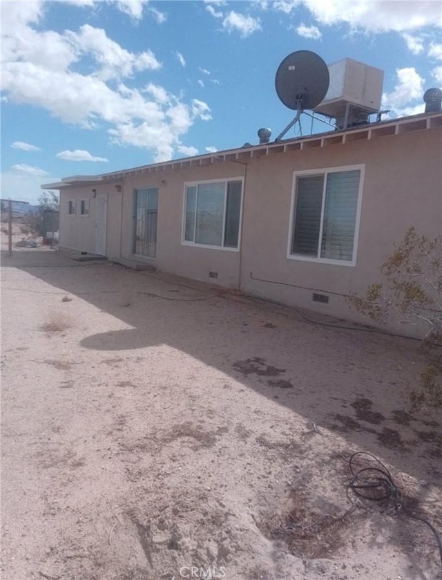 rear view of property featuring crawl space and stucco siding