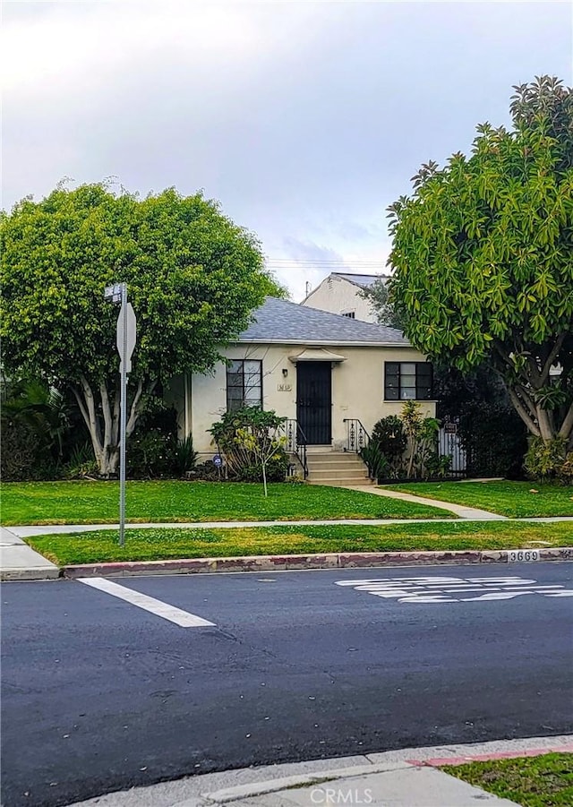 view of front of house featuring stucco siding, a front yard, and roof with shingles