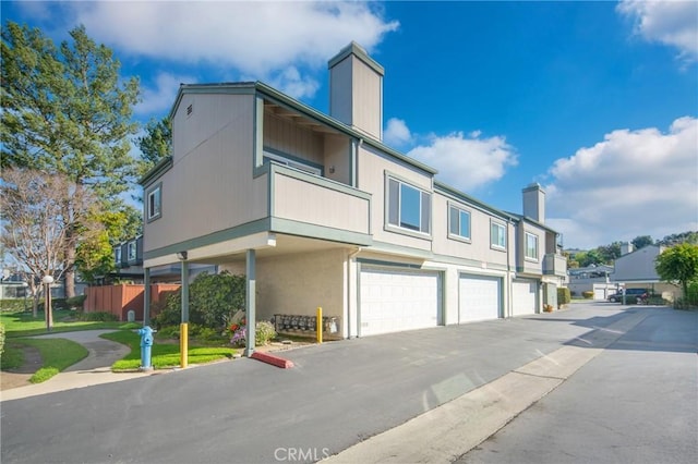 exterior space featuring stucco siding, an attached garage, aphalt driveway, and a chimney