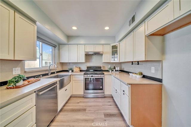 kitchen with recessed lighting, a sink, light wood-style floors, under cabinet range hood, and appliances with stainless steel finishes