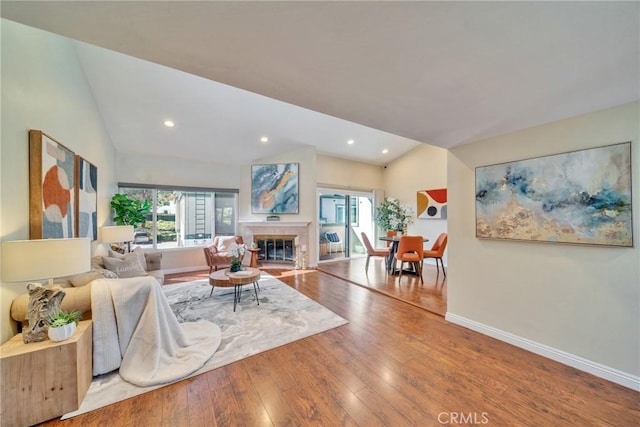 living room featuring baseboards, lofted ceiling, a tiled fireplace, and hardwood / wood-style flooring