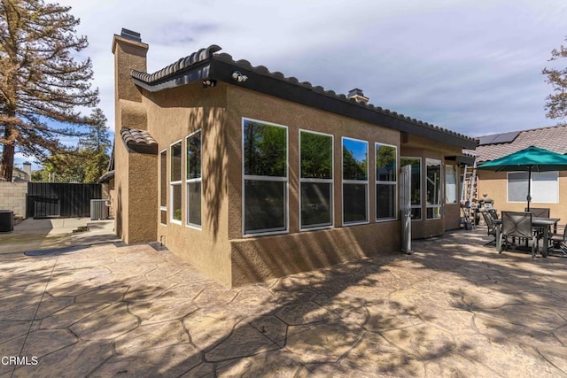 back of house featuring fence, central AC unit, a chimney, outdoor dining area, and a patio