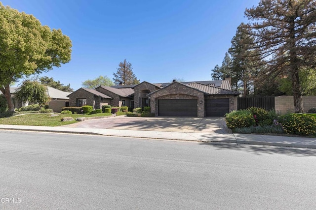 view of front of home featuring solar panels, fence, concrete driveway, stone siding, and an attached garage