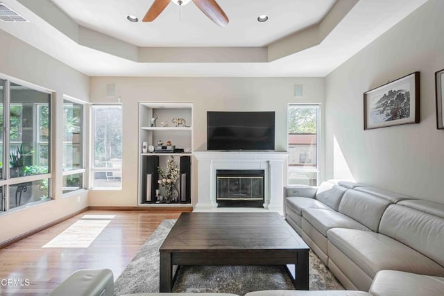 living area with a raised ceiling, built in features, a ceiling fan, and visible vents