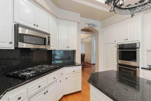 kitchen with light wood-style flooring, arched walkways, decorative backsplash, white cabinets, and appliances with stainless steel finishes