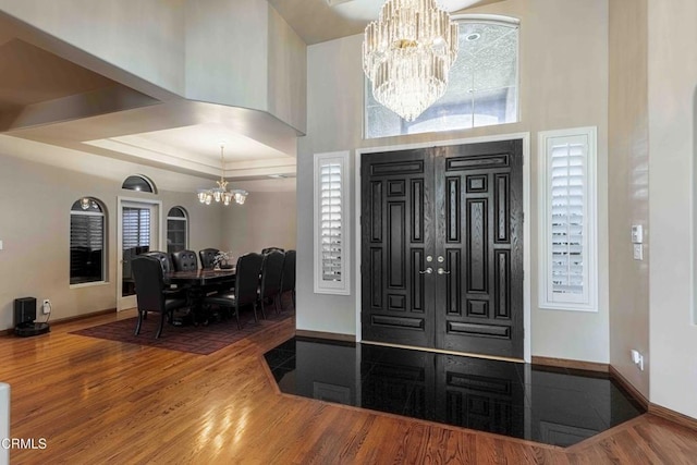 entrance foyer featuring an inviting chandelier, wood finished floors, baseboards, and a towering ceiling