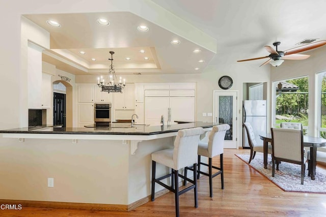 kitchen featuring dark countertops, light wood-type flooring, appliances with stainless steel finishes, white cabinets, and a raised ceiling