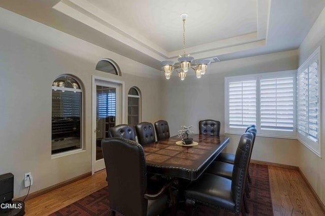 dining room featuring a notable chandelier, a raised ceiling, baseboards, and wood finished floors