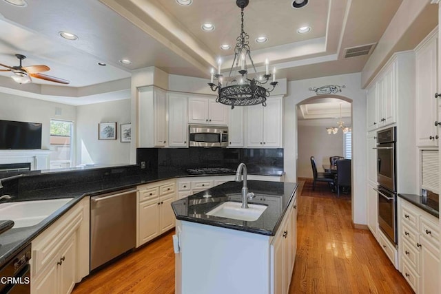 kitchen with a sink, a tray ceiling, arched walkways, appliances with stainless steel finishes, and light wood finished floors