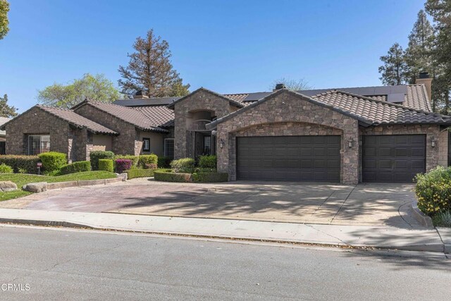 view of front of home with stone siding, an attached garage, a chimney, and a tiled roof