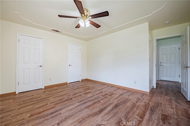 unfurnished bedroom featuring a ceiling fan, wood finished floors, visible vents, and baseboards