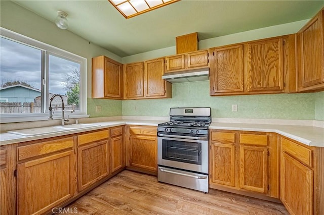 kitchen featuring light wood-type flooring, under cabinet range hood, a sink, stainless steel range with gas cooktop, and light countertops