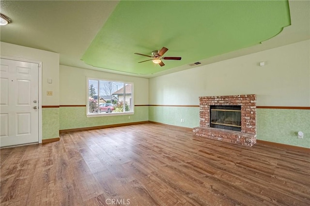 unfurnished living room with visible vents, wood finished floors, a fireplace, baseboards, and ceiling fan