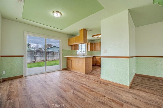 kitchen featuring light wood-type flooring, a peninsula, a sink, light countertops, and brown cabinets