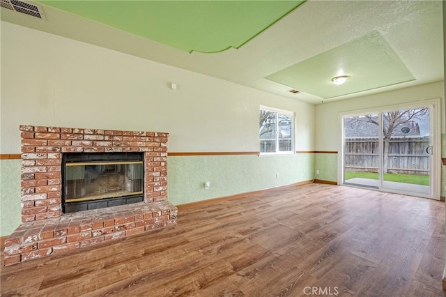 unfurnished living room featuring a fireplace, wood finished floors, visible vents, and baseboards