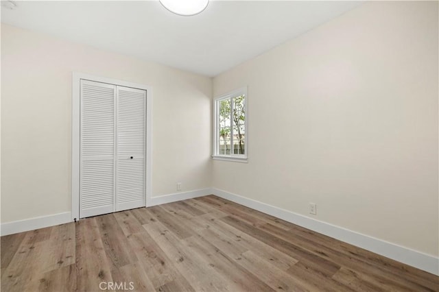 unfurnished bedroom with light wood-style flooring, baseboards, and a closet