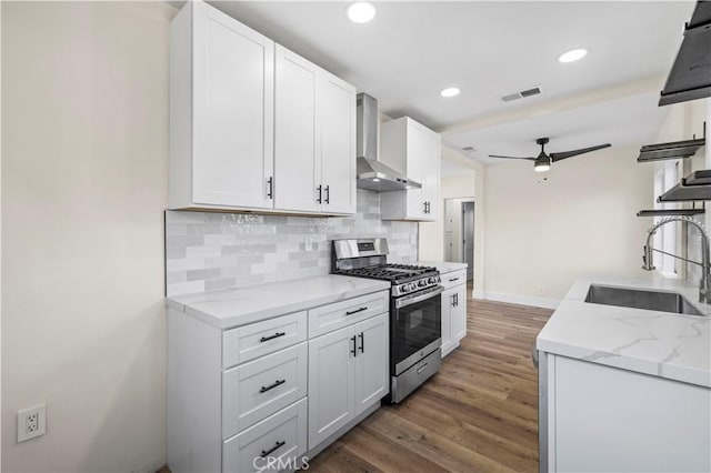 kitchen featuring visible vents, a sink, tasteful backsplash, gas stove, and wall chimney exhaust hood