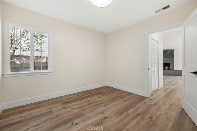 spare room featuring a lit fireplace, visible vents, light wood-type flooring, and baseboards