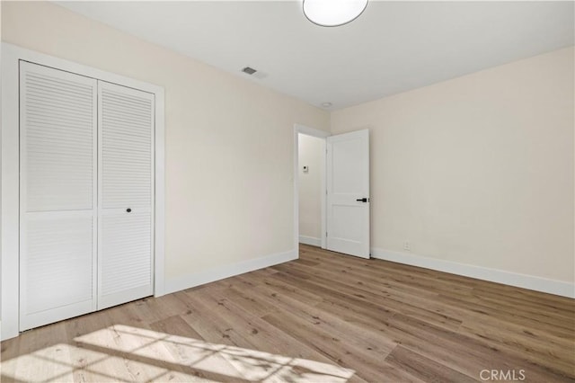 unfurnished bedroom featuring a closet, visible vents, baseboards, and wood finished floors