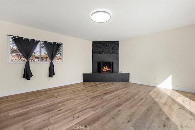 unfurnished living room with wood finished floors, a fireplace, and baseboards