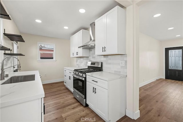 kitchen with open shelves, a sink, gas range, wall chimney range hood, and tasteful backsplash