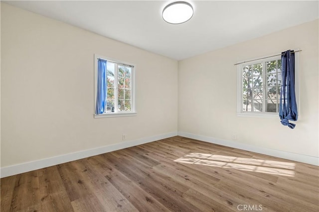 spare room featuring plenty of natural light, wood finished floors, and baseboards