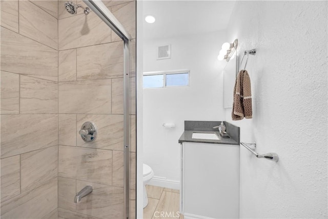 bathroom with vanity, baseboards, visible vents, a tile shower, and toilet