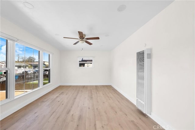 unfurnished room featuring a ceiling fan, a heating unit, light wood finished floors, and baseboards