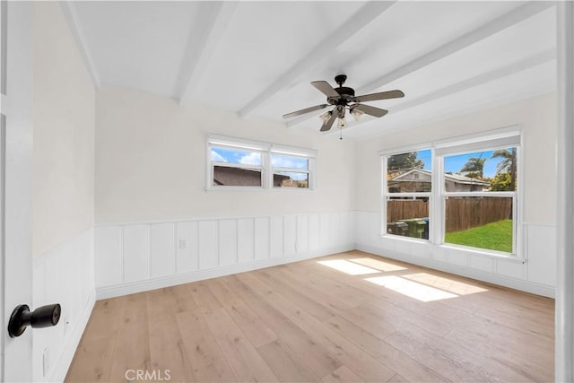 spare room with beam ceiling, plenty of natural light, and wainscoting