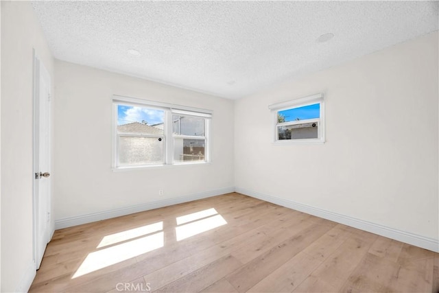 empty room with light wood-type flooring, baseboards, and a textured ceiling