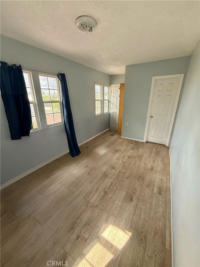 spare room with a textured ceiling, baseboards, and light wood-style flooring