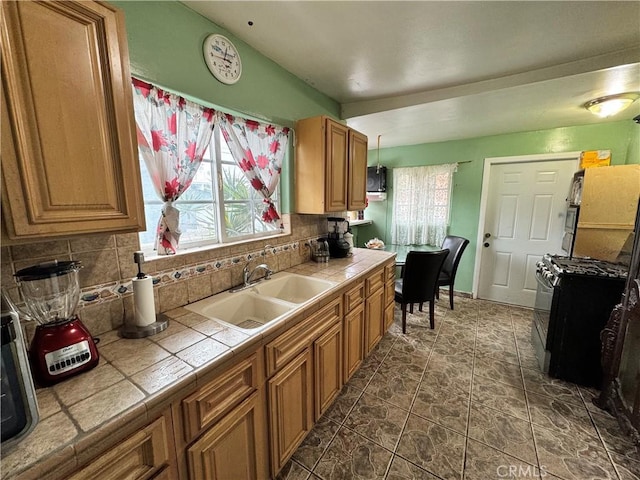 kitchen featuring a sink, tile counters, plenty of natural light, decorative backsplash, and range with gas cooktop