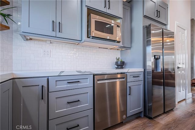 kitchen featuring stainless steel appliances, decorative backsplash, dark wood finished floors, and gray cabinets