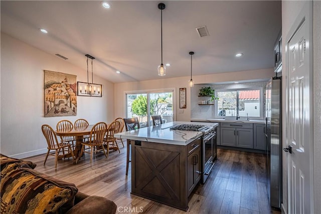 kitchen with dark wood-type flooring, appliances with stainless steel finishes, a breakfast bar area, light countertops, and vaulted ceiling